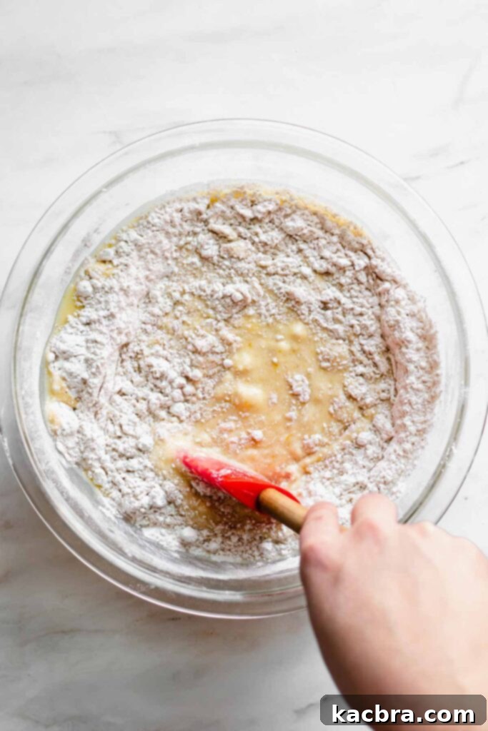 Wet ingredients being gently folded into the dry ingredients with a rubber spatula, creating a slightly lumpy batter for jumbo blueberry muffins.