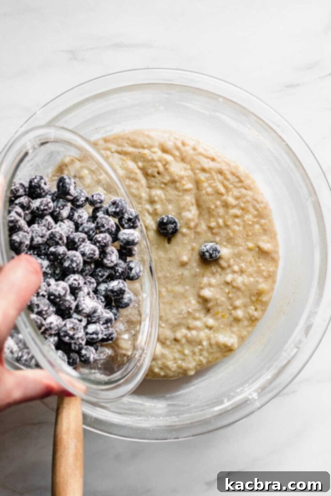 Floured blueberries being poured into the muffin batter, ready for a final gentle fold.