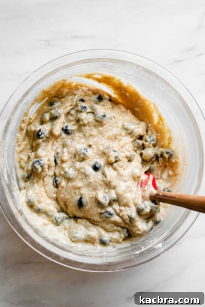 Blueberries being gently folded into the muffin batter with a rubber spatula, ensuring even distribution without crushing them.