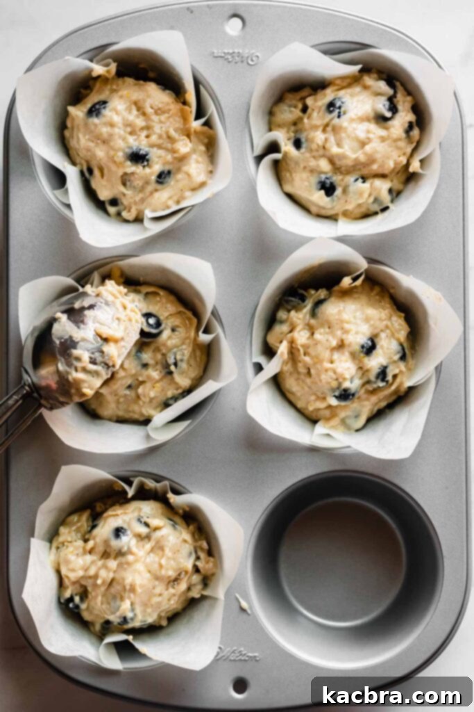 Muffin batter being expertly scooped into muffin wells with a large cookie scoop, filling them generously.