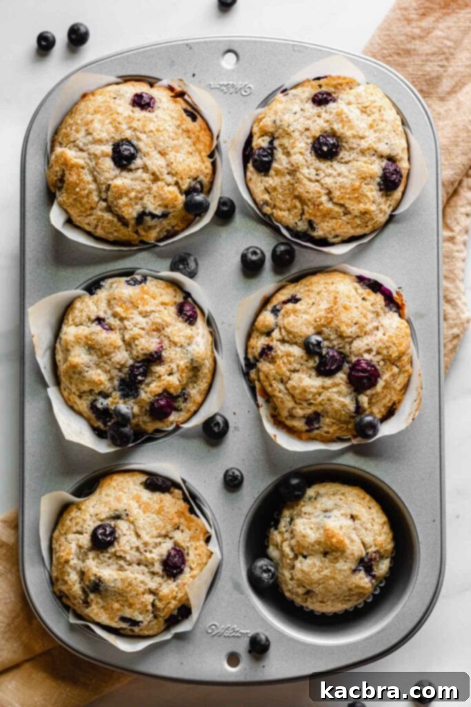 Five perfectly baked jumbo muffins and one regular sized muffin in a muffin tin, showcasing their golden-brown tops and generous rise.