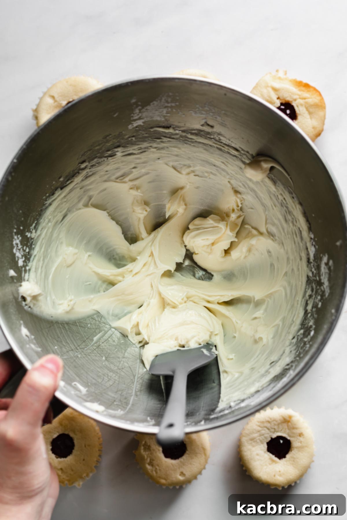 Double Strawberry Crunch Cupcakes 14 Cold cream cheese, powdered sugar, and vanilla being creamed together in a stand mixer bowl, with the sides scraped down for even mixing.