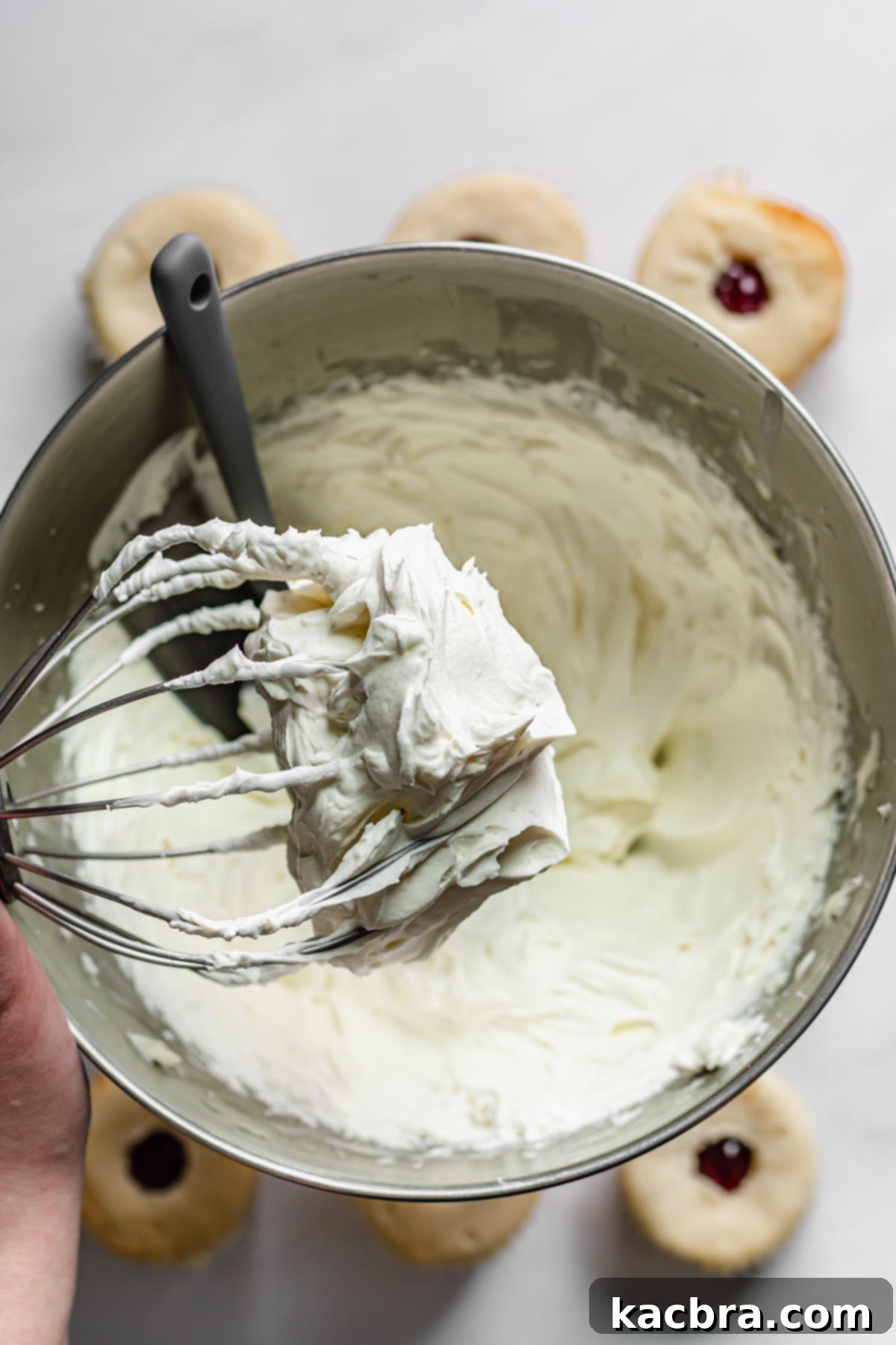 Double Strawberry Crunch Cupcakes 16 The whipped cream cheese frosting exhibiting stiff peaks on the tip of a whisk attachment, indicating its perfect, airy consistency.