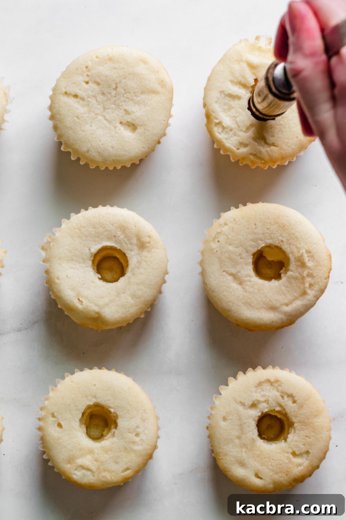 Double Strawberry Crunch Cupcakes 17 The handle of a wooden spoon gently pressing into the center of a baked cupcake, creating a perfect hole for filling.