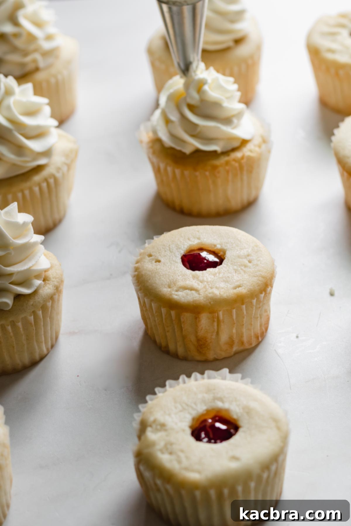Double Strawberry Crunch Cupcakes 19 A row of cupcakes in various stages of frosting, some already filled with jam, while others are being adorned with a perfect swirl of whipped cream cheese frosting.