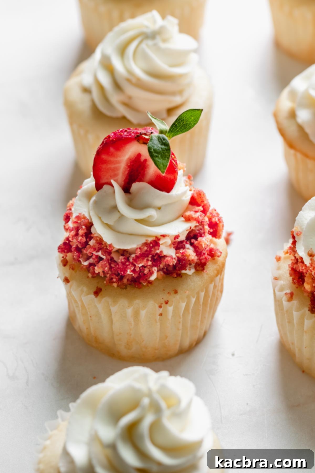 Double Strawberry Crunch Cupcakes 20 A beautifully decorated strawberry crunch cupcake, adorned with its signature crumble and a fresh strawberry, standing out among other frosted cupcakes.