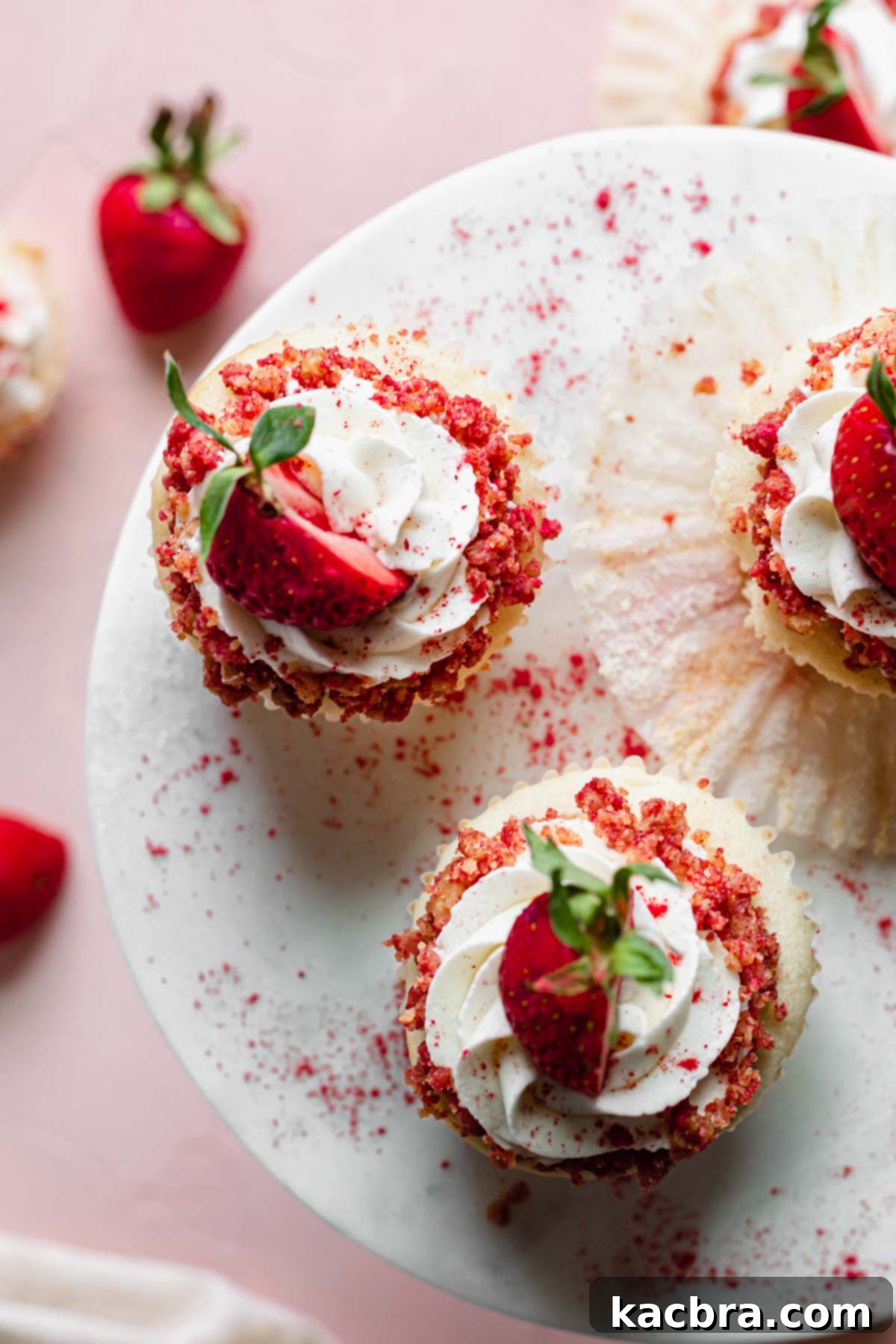 Double Strawberry Crunch Cupcakes 21 An overhead shot of three exquisitely decorated strawberry crunch cupcakes resting on a elegant cake stand, highlighting their vibrant topping and fresh strawberry garnishes.