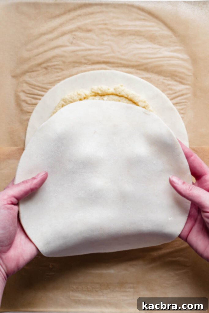 Hands carefully position the second pastry circle evenly over the first, enclosing the almond cream.