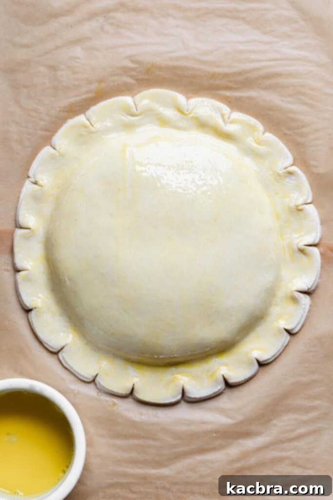 The pastry, freshly brushed with the first layer of egg wash, displays a faint yellow hue.