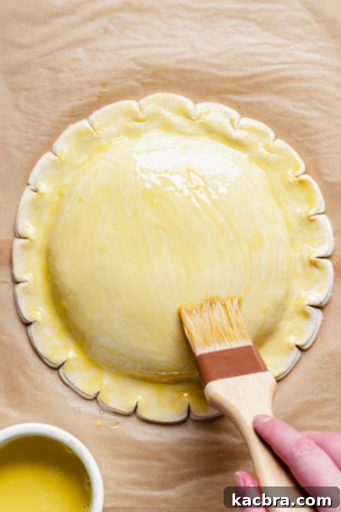 A pastry brush skillfully applies the second round of egg wash to the chilled galette.