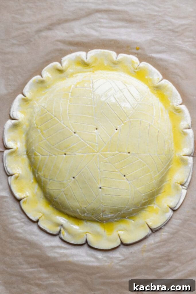 An overhead shot of the Galette des Rois, expertly scored with a design and punctured with steam release holes, pre-baking.