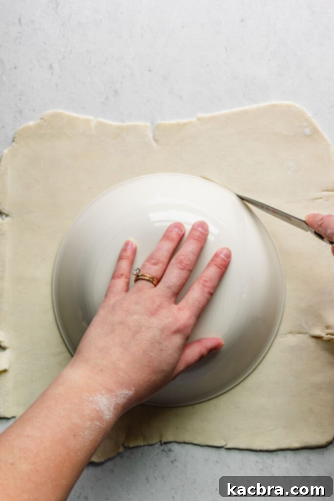 A bowl is placed on rolled out rough puff pastry, with a knife carefully cutting along its edge to form a perfect circle.