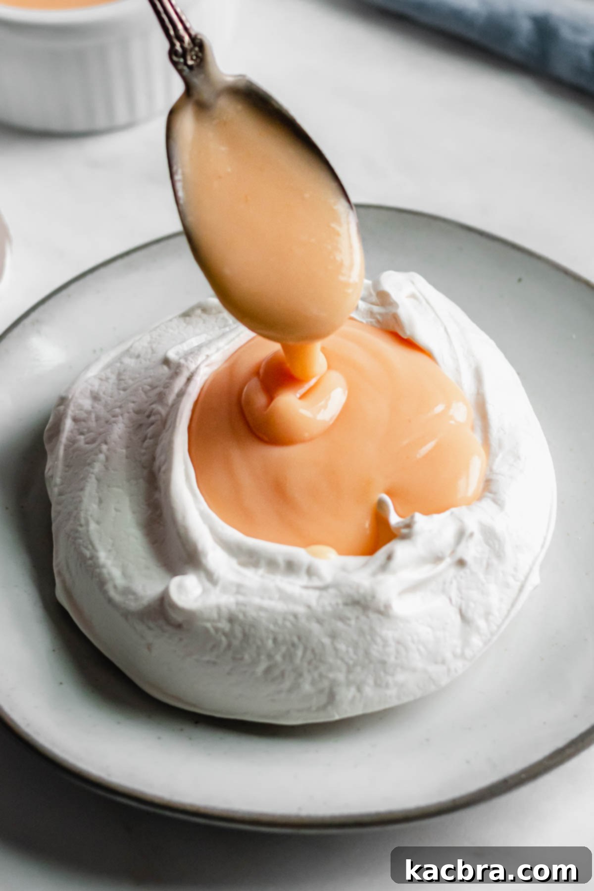Crisp Meringue Nests with Bright Grapefruit Curd 13 A spoon gracefully pours the shimmering grapefruit curd into the crisp hollow of a mini pavlova nest, preparing it for its fresh fruit topping.