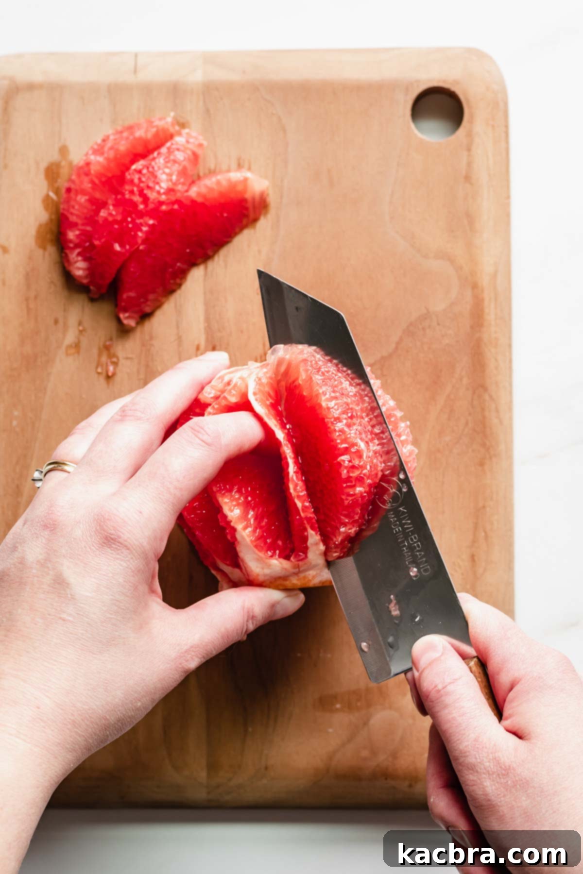 Crisp Meringue Nests with Bright Grapefruit Curd 14 A sharp knife meticulously slices into a segment of fresh grapefruit, skillfully separating it from the membrane to create a perfect, juicy garnish for the dessert.