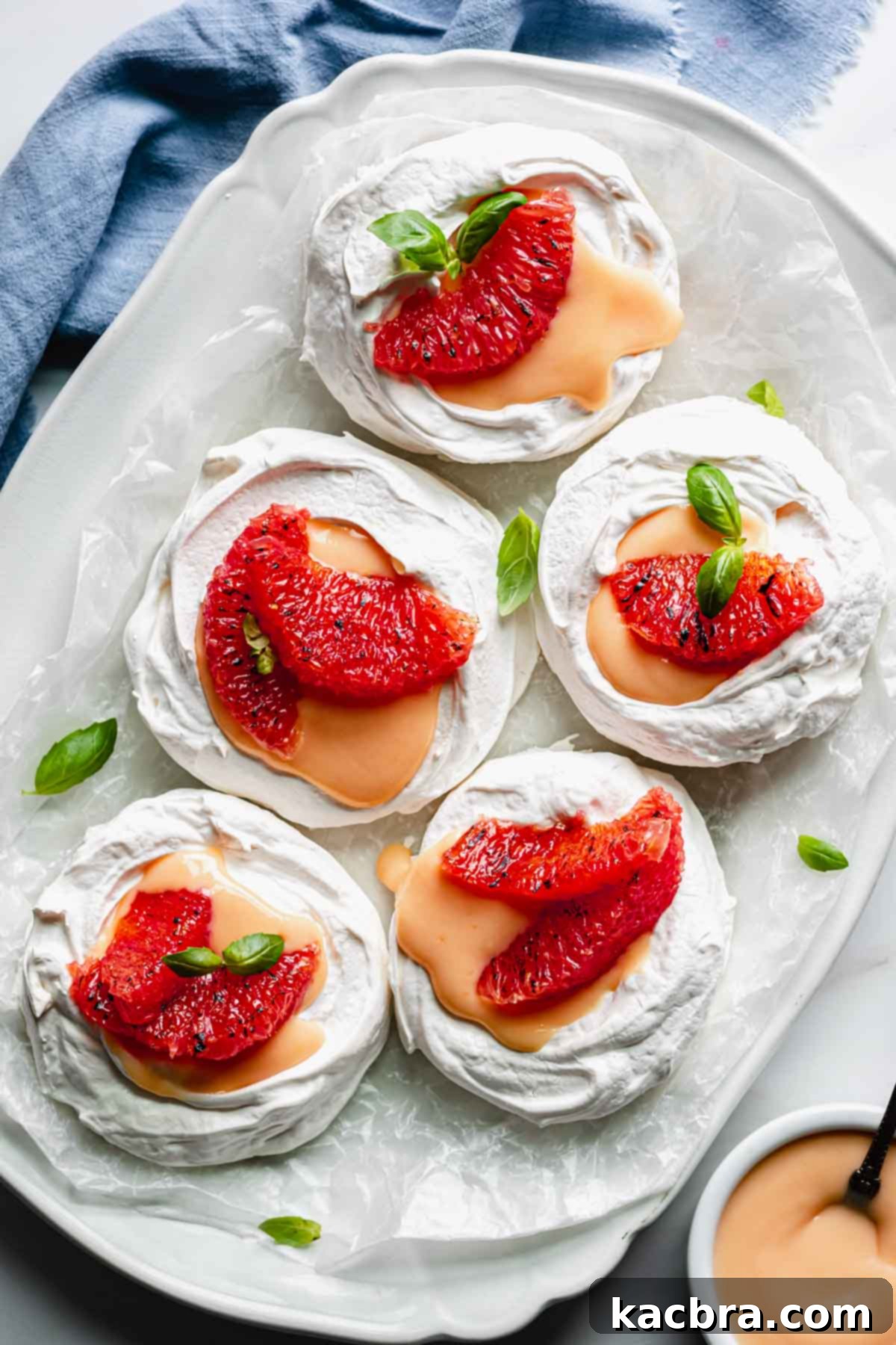Crisp Meringue Nests with Bright Grapefruit Curd 15 A stunning platter showcasing five perfectly assembled mini pavlova nests, each generously filled with grapefruit curd and garnished with fresh grapefruit segments and delicate basil leaves, creating a beautiful presentation.