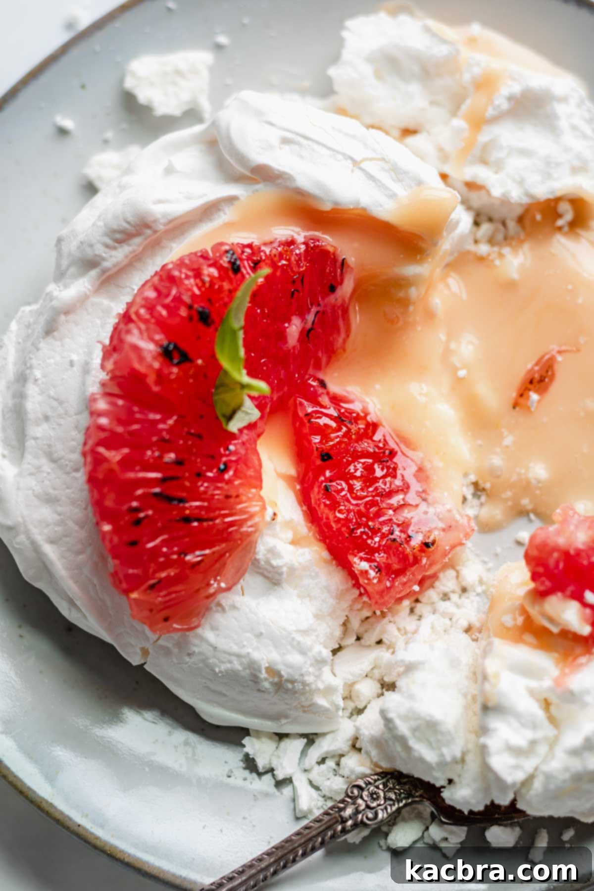 Crisp Meringue Nests with Bright Grapefruit Curd 16 A close-up view of a mini pavlova nest, gently broken open to reveal its luscious grapefruit curd filling and the crisp, airy meringue. Two vibrant grapefruit segments rest elegantly on top, adding a fresh touch.