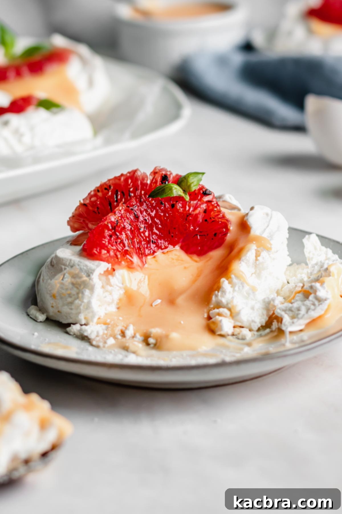 Crisp Meringue Nests with Bright Grapefruit Curd 3 A single, beautifully crafted pavlova nest resting on a plate, with a delicate bite taken from its side, revealing the creamy grapefruit curd and the meringue's soft, marshmallow-like center.