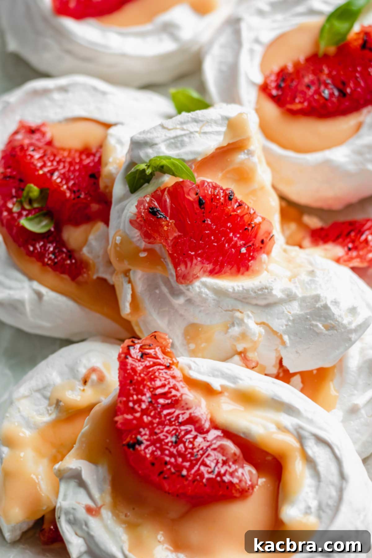 Crisp Meringue Nests with Bright Grapefruit Curd 4 A charming stack of freshly baked mini pavlovas, with one slightly broken nest artfully placed on top, showcasing the delicate, airy structure of the meringue.