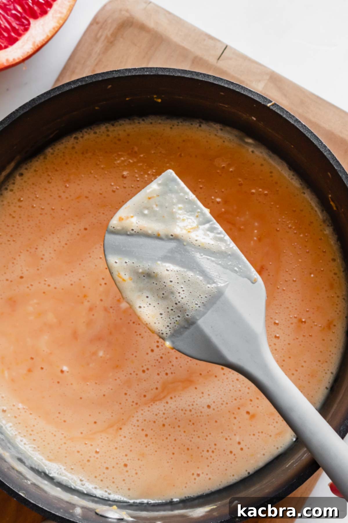 Crisp Meringue Nests with Bright Grapefruit Curd 6 A rubber spatula is lifted from the saucepan, displaying a thick, creamy layer of grapefruit curd, indicating it has reached the perfect consistency.