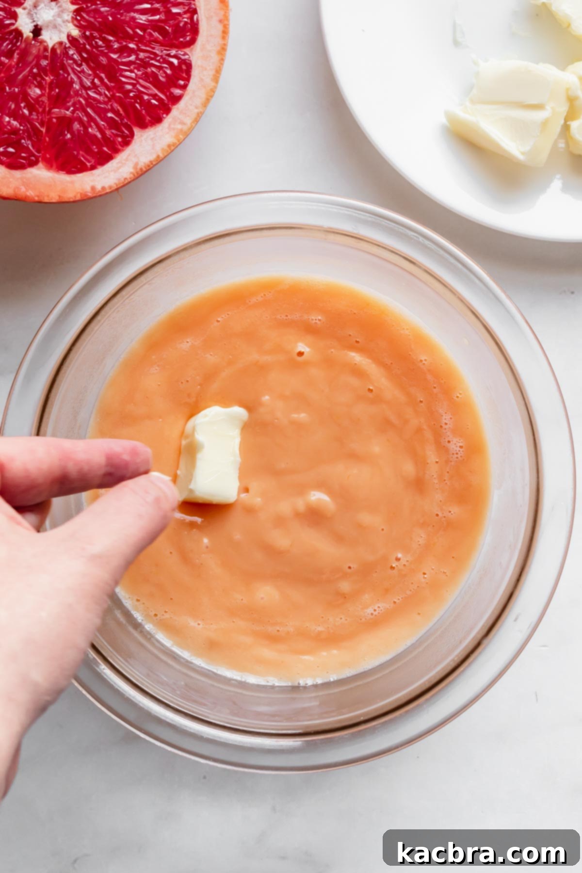 Crisp Meringue Nests with Bright Grapefruit Curd 8 Softened, unsalted butter cubes are gently dropped into the warm, silky grapefruit curd in a bowl, ready to be whisked in for richness and smoothness.
