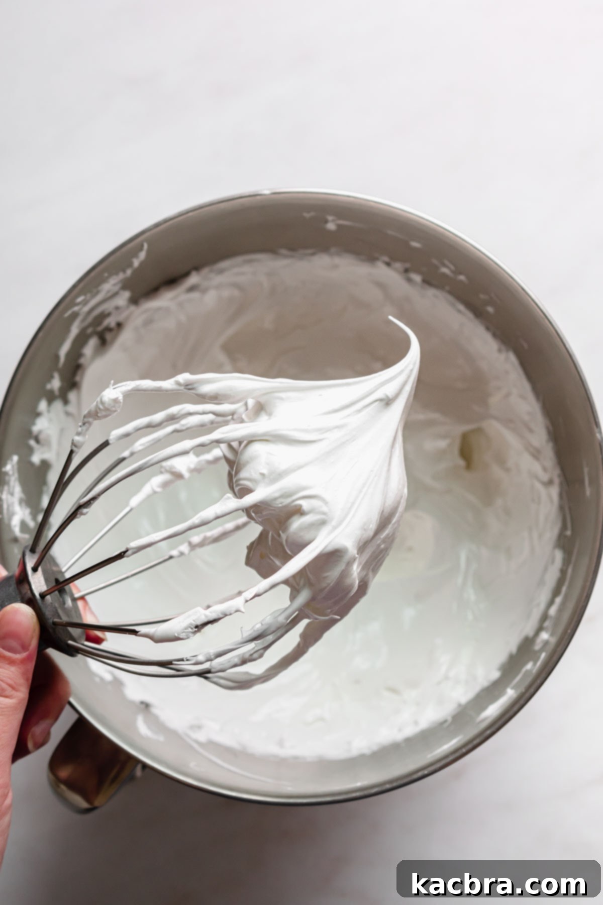 Crisp Meringue Nests with Bright Grapefruit Curd 10 A whisk is held aloft over a mixing bowl, showcasing the perfectly stiff peaks of the Swiss meringue, a clear sign of its readiness.