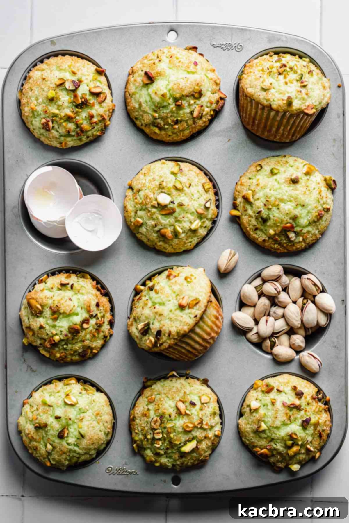 Freshly baked pistachio muffins in a pan, with empty wells around them holding discarded eggshells and pistachio remnants.