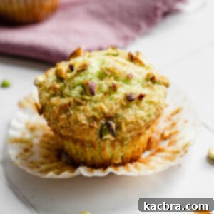 One pistachio muffin with the liner pulled down, showing its green interior and crunchy top.