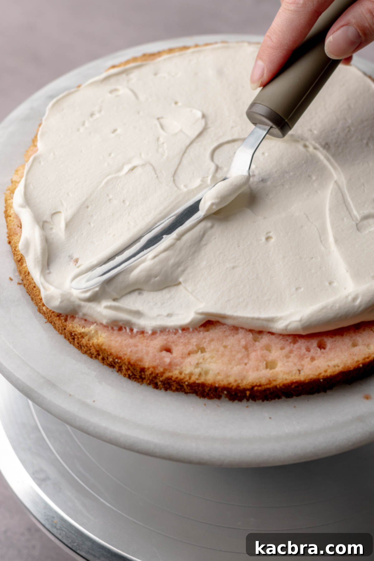 A spatula spreading whipped cream onto a cake layer.
