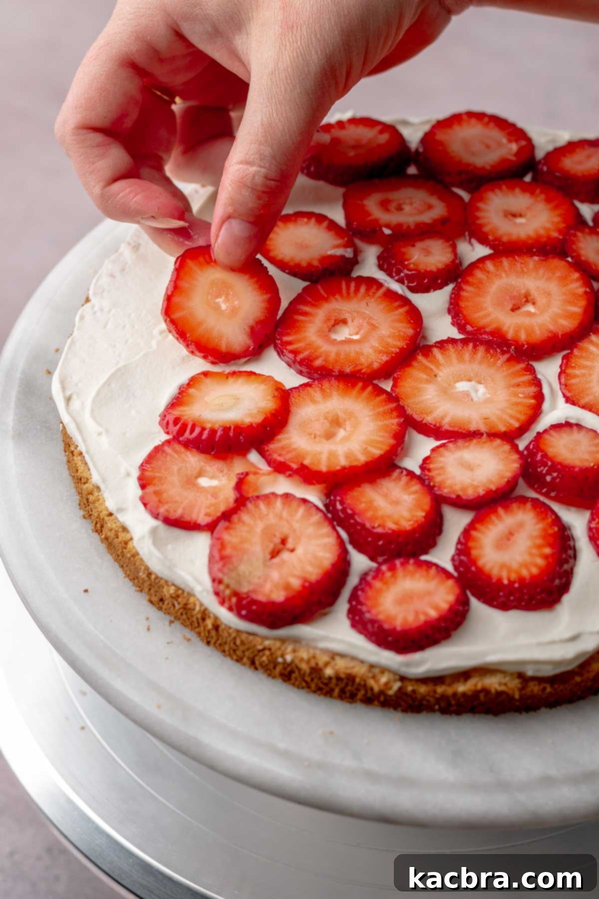 A hand adding sliced strawberries to the whipped cream layer.