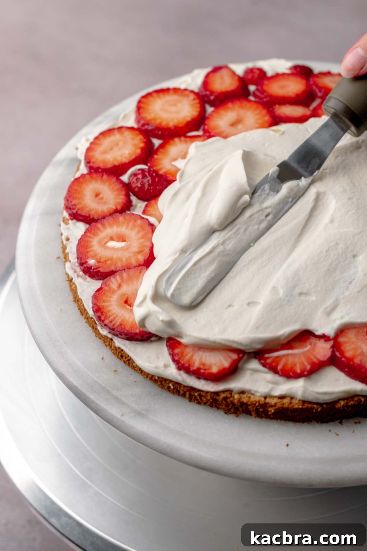 A spatula spreading whipped cream on top of strawberries.