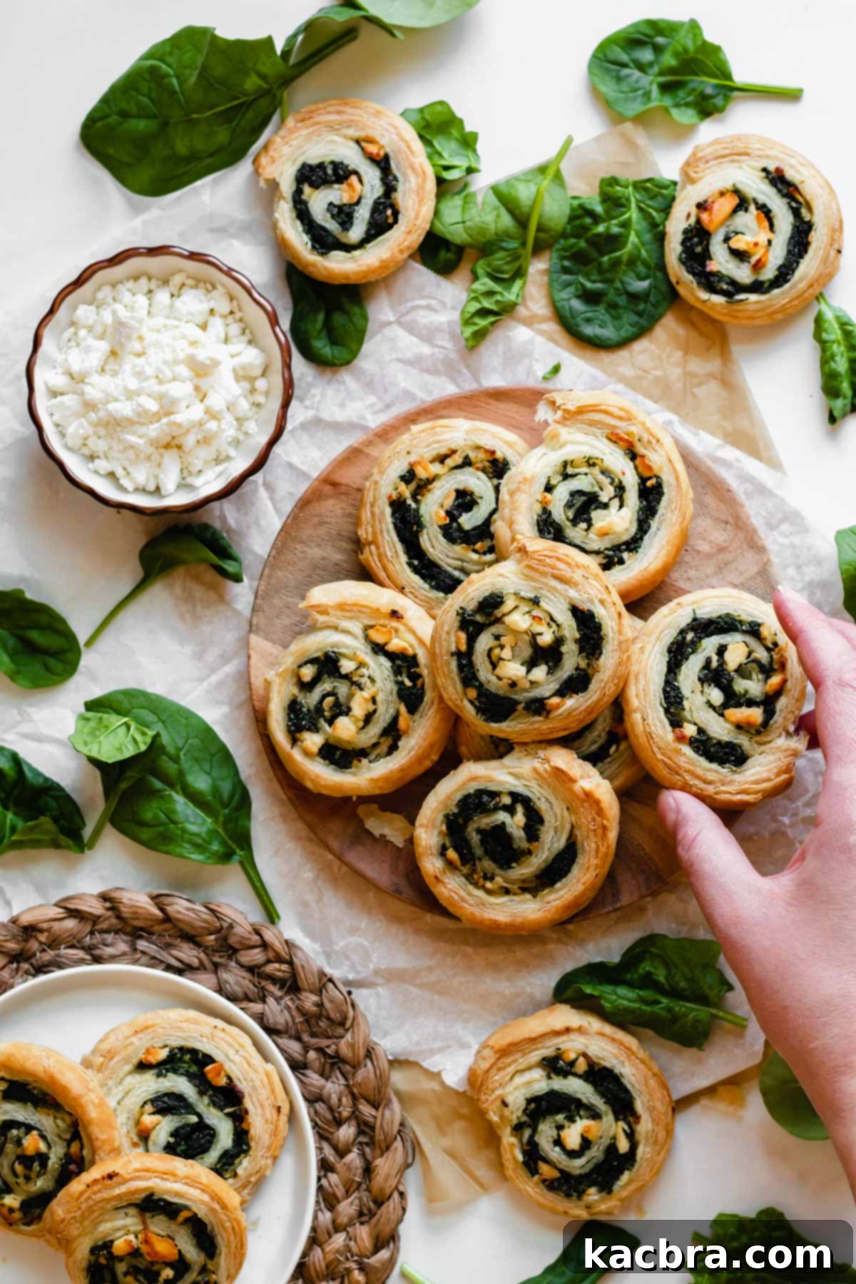 Spinach and feta pinwheels artfully layered on a white plate, with a hand reaching for one.