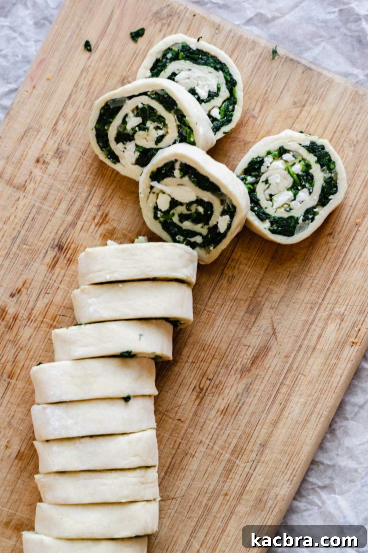 Slicing the chilled spinach and feta pastry log into individual pinwheels with a serrated knife.