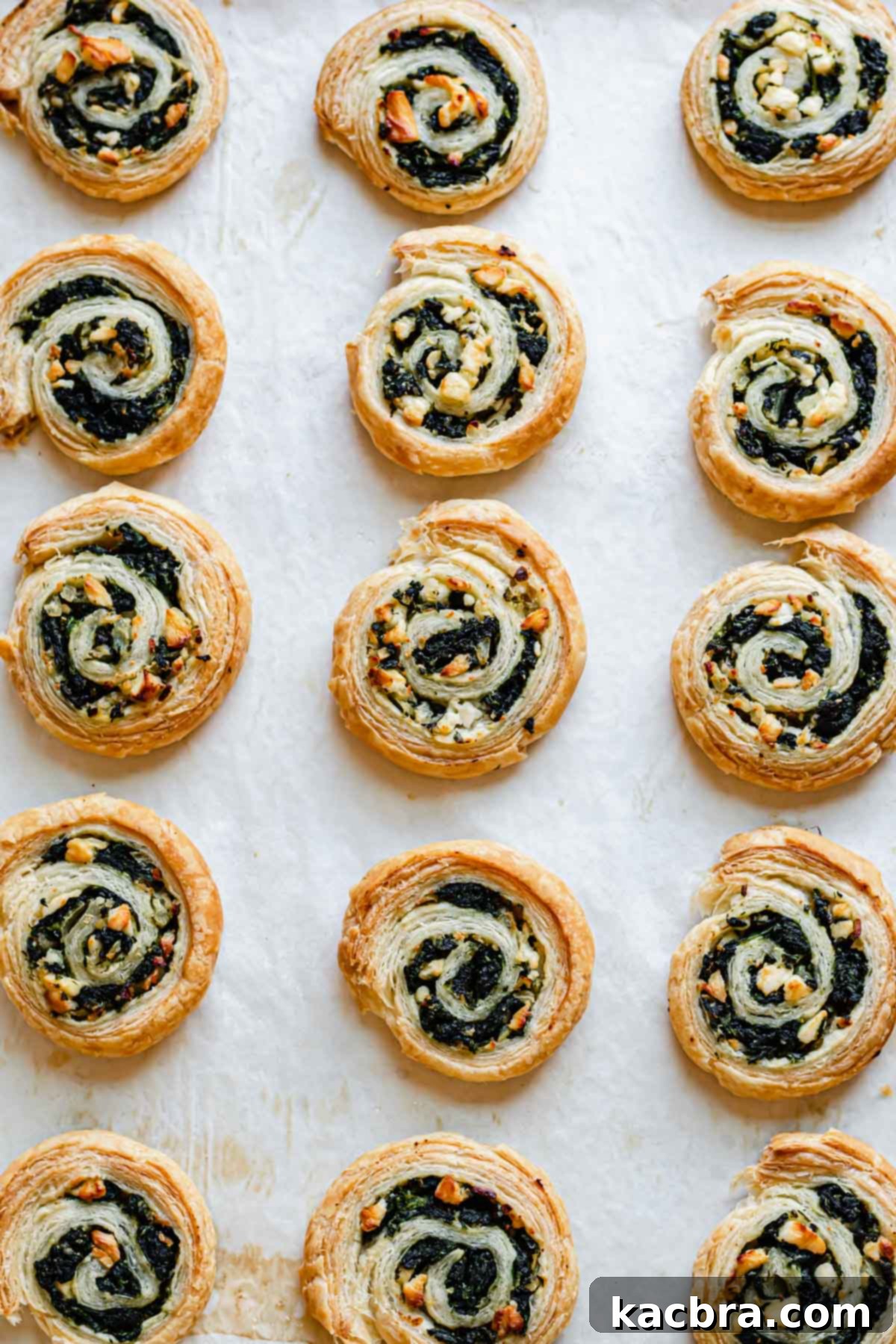 Golden-brown, baked spinach and feta pinwheels resting on a parchment-lined baking tray.