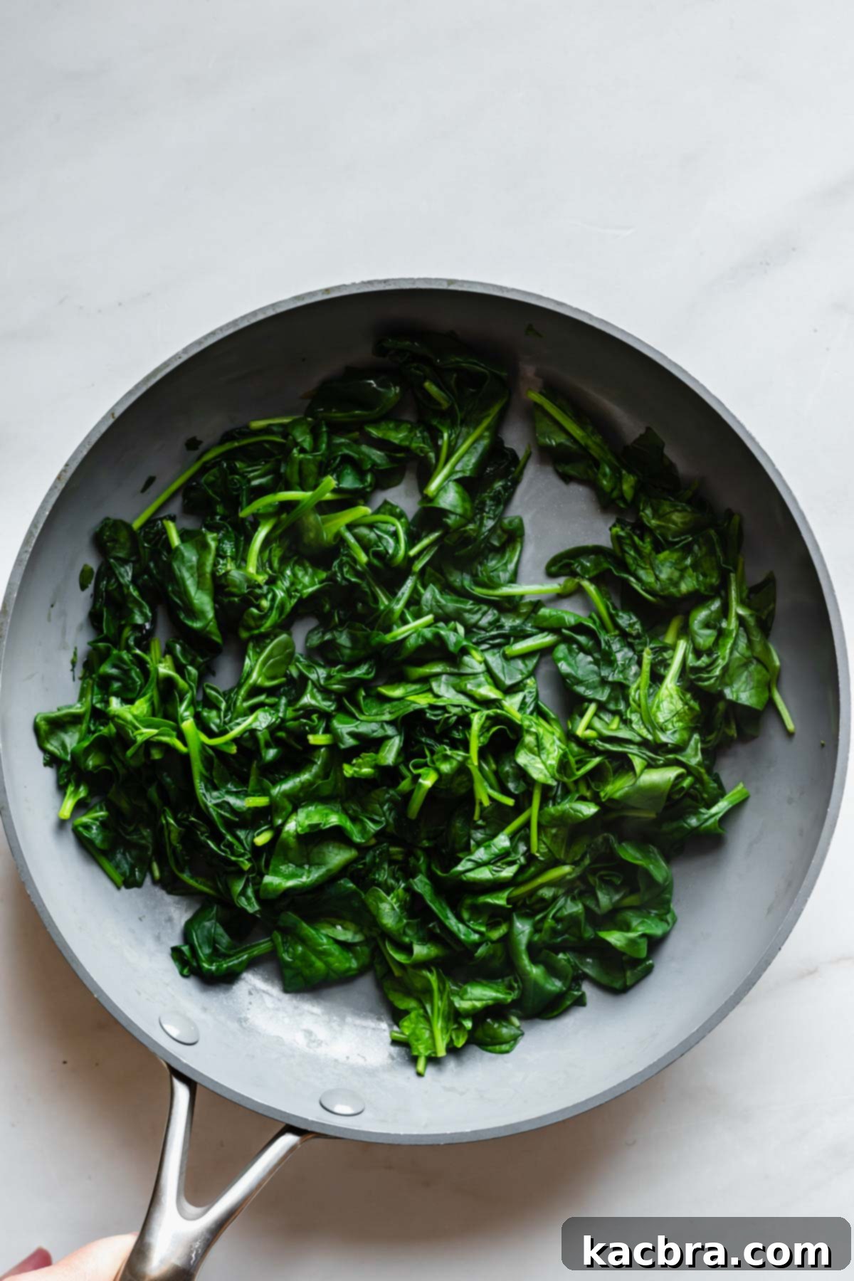 Fresh spinach wilting in a pan over medium heat.