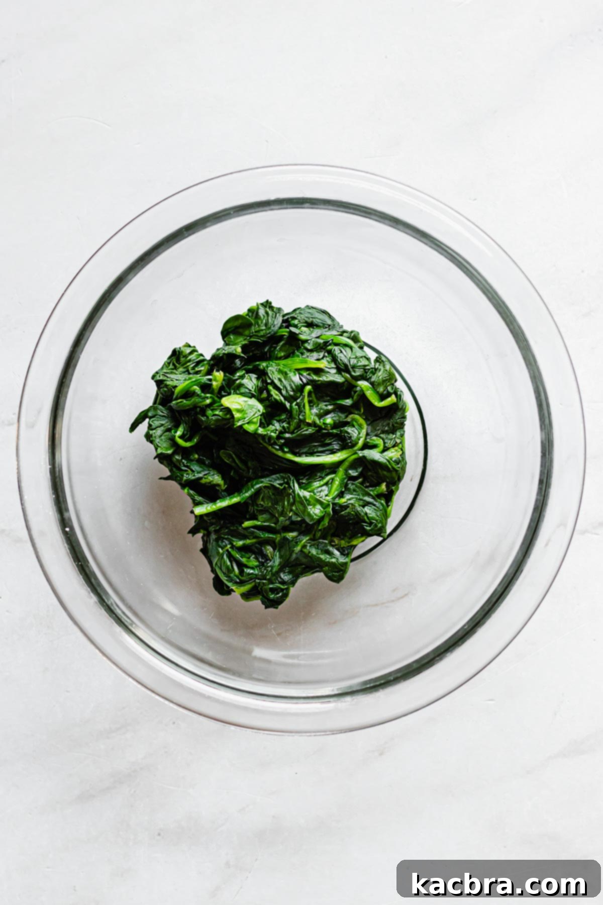 A tightly squeezed ball of wilted spinach in a bowl, demonstrating excess liquid removal.