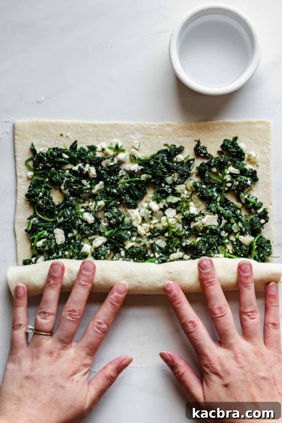 The puff pastry being rolled up tightly with the spinach and feta filling inside.