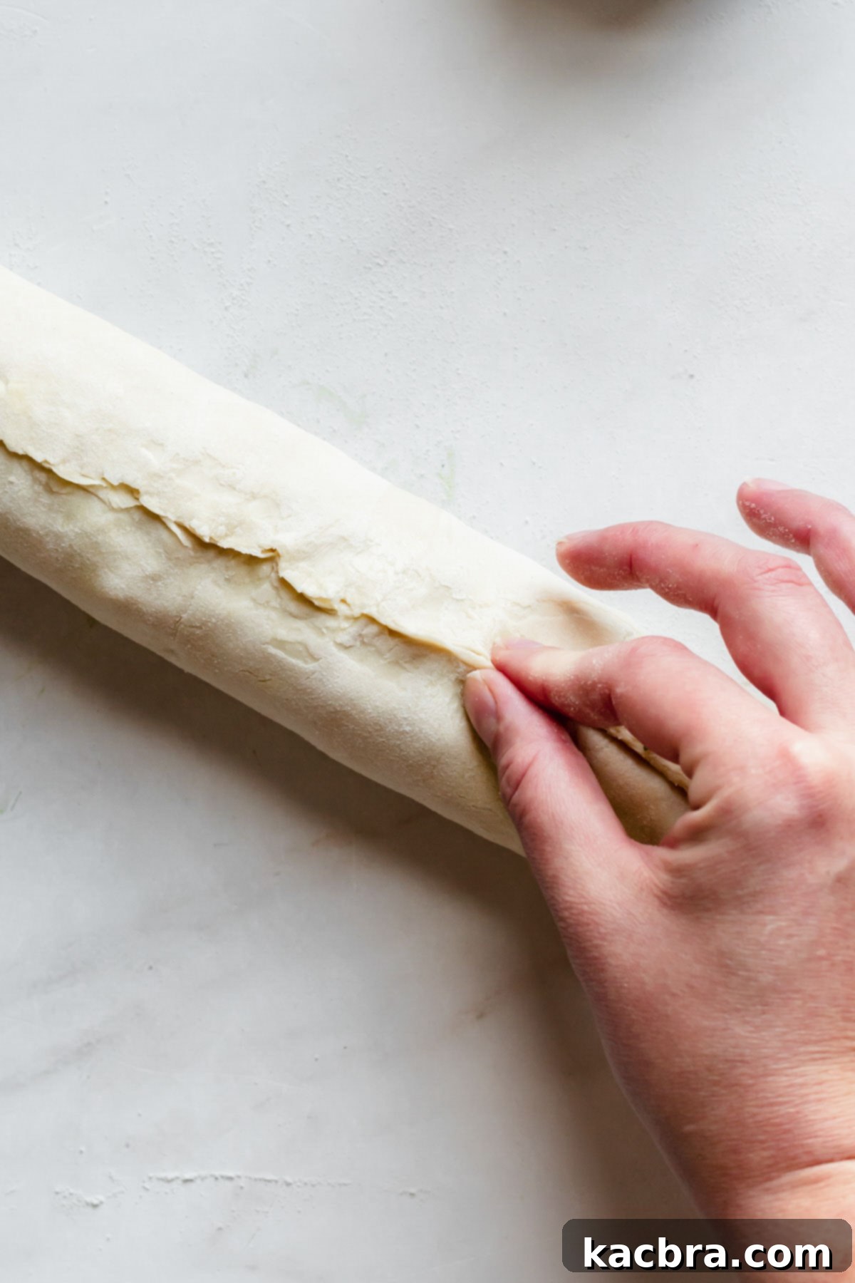 A hand pinching the seam of the rolled puff pastry to seal it completely.