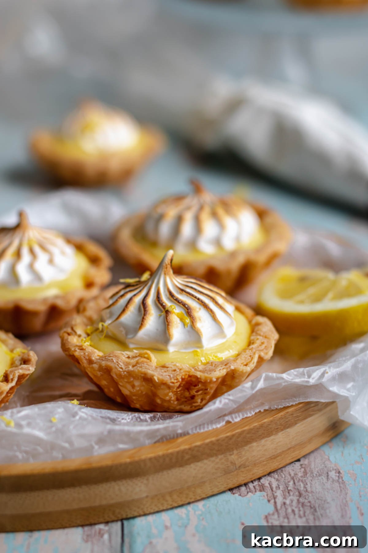 Zingy Lemon Meringue Kisses 3 Close-up of golden brown mini lemon meringue tartlets on a white platter.