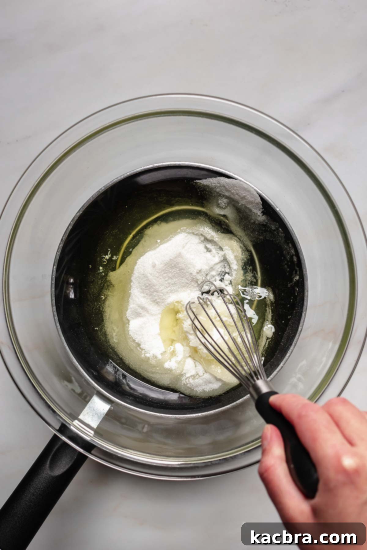 Zingy Lemon Meringue Kisses 6 A hand whisking egg whites and sugar in a bowl set over a pot of simmering water (bain-marie).