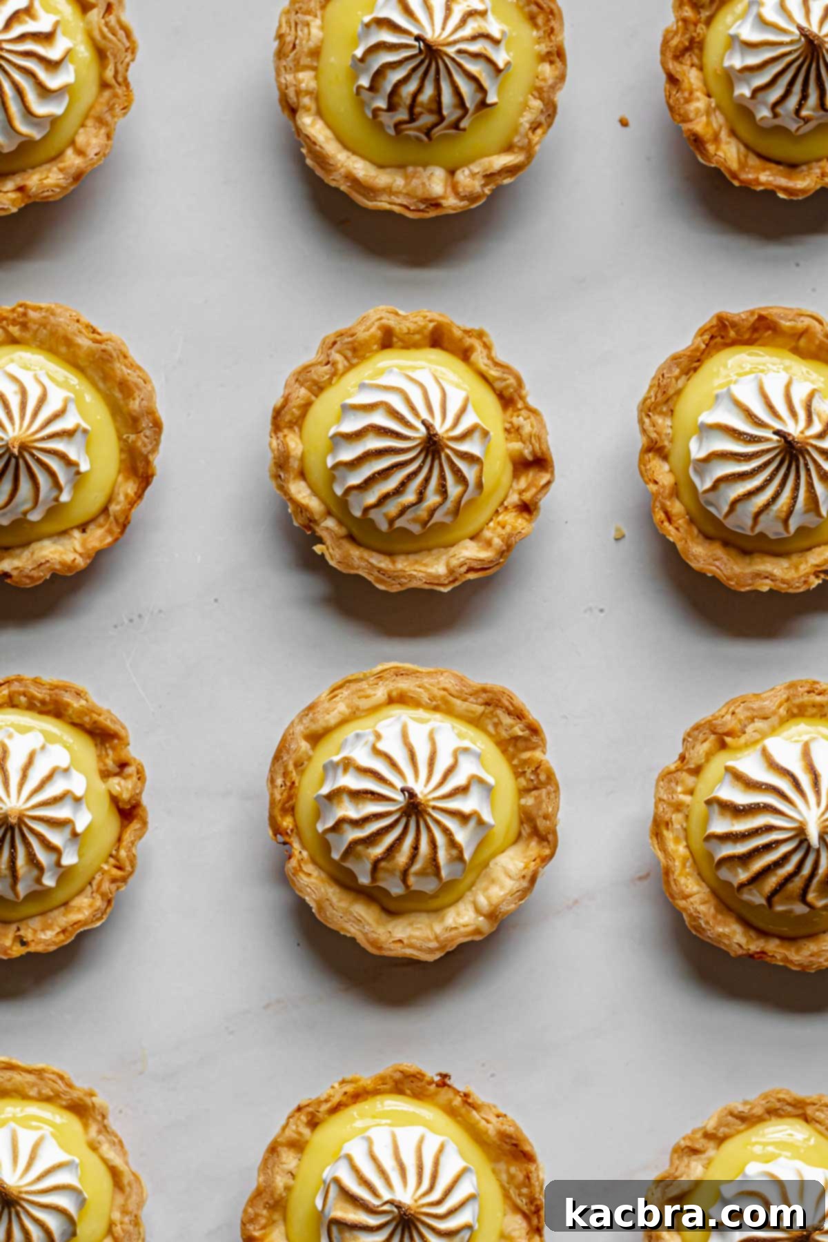 Zingy Lemon Meringue Kisses 9 Several finished mini lemon meringue tarts, perfectly toasted, lined up on a tray.