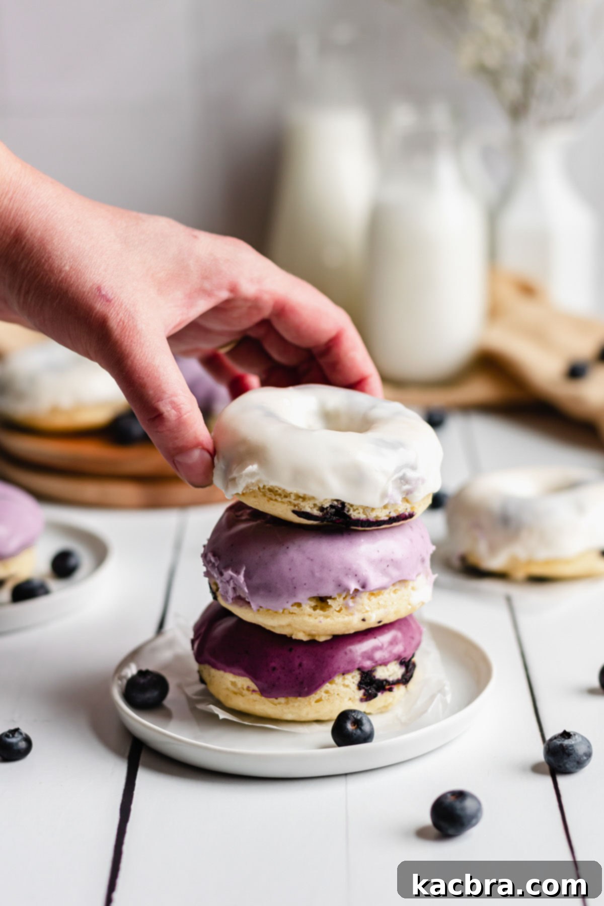 Oven-Fresh Blueberry Glazed Rounds 3 A hand reaches in to remove the top donut from a stack.
