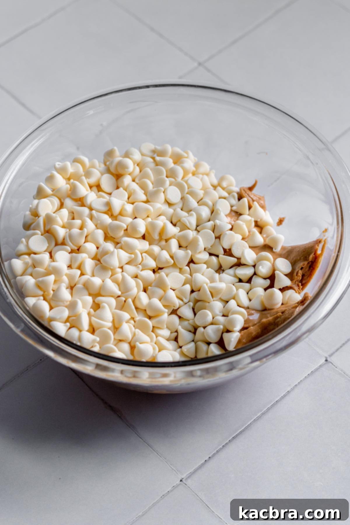 Decadent Fluffernutter Fudge 5 White chocolate chips being added on top of the peanut butter in a bowl.