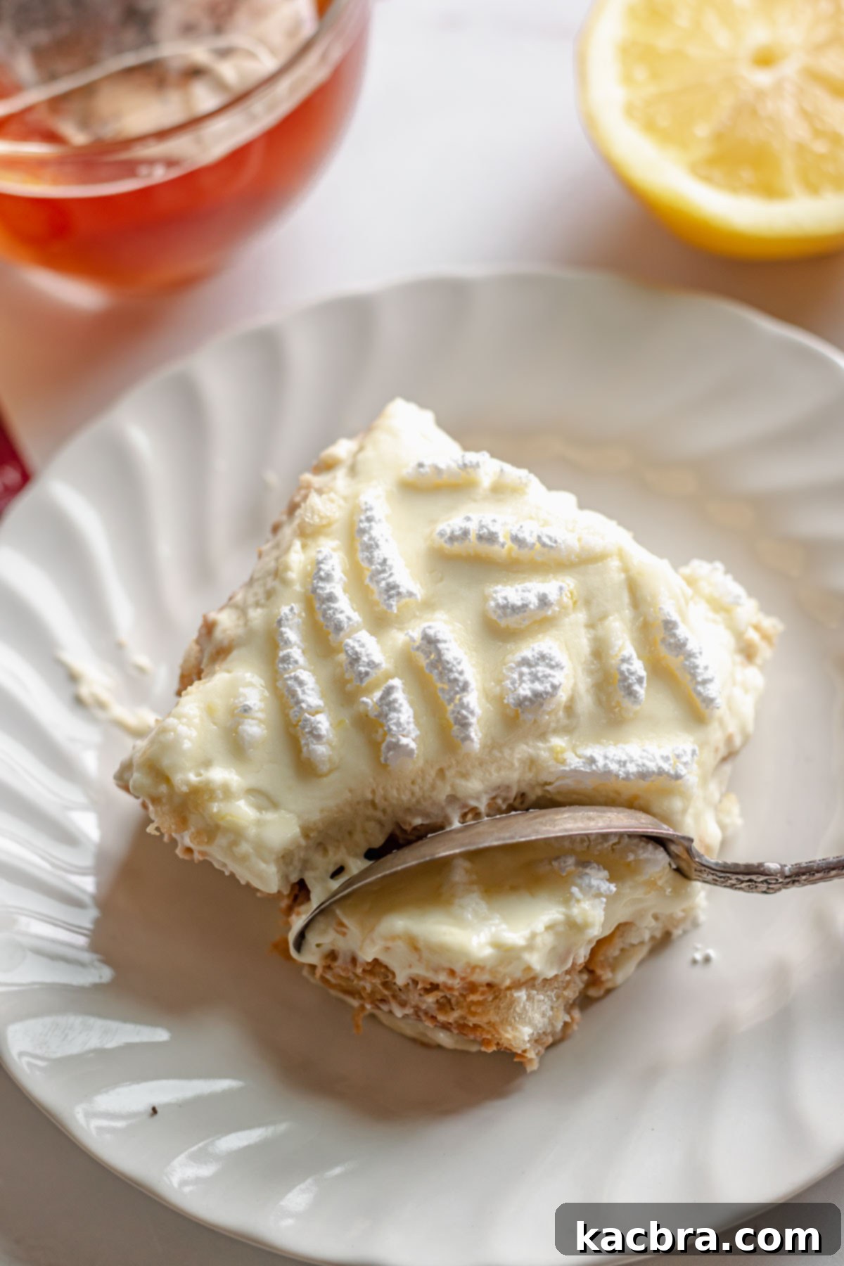 Slice of tiramisu on a plate with a spoon removing a corner, showcasing layers of tea-soaked ladyfingers and lemon mascarpone cream.