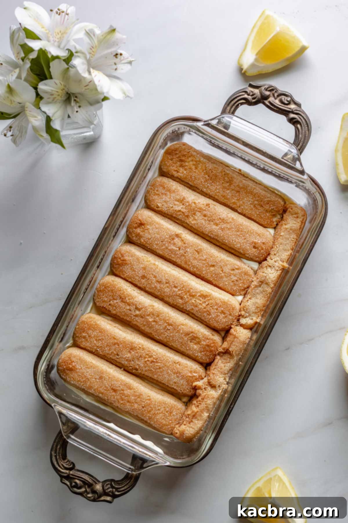 Adding the second layer of dipped lady fingers on top of the cream.