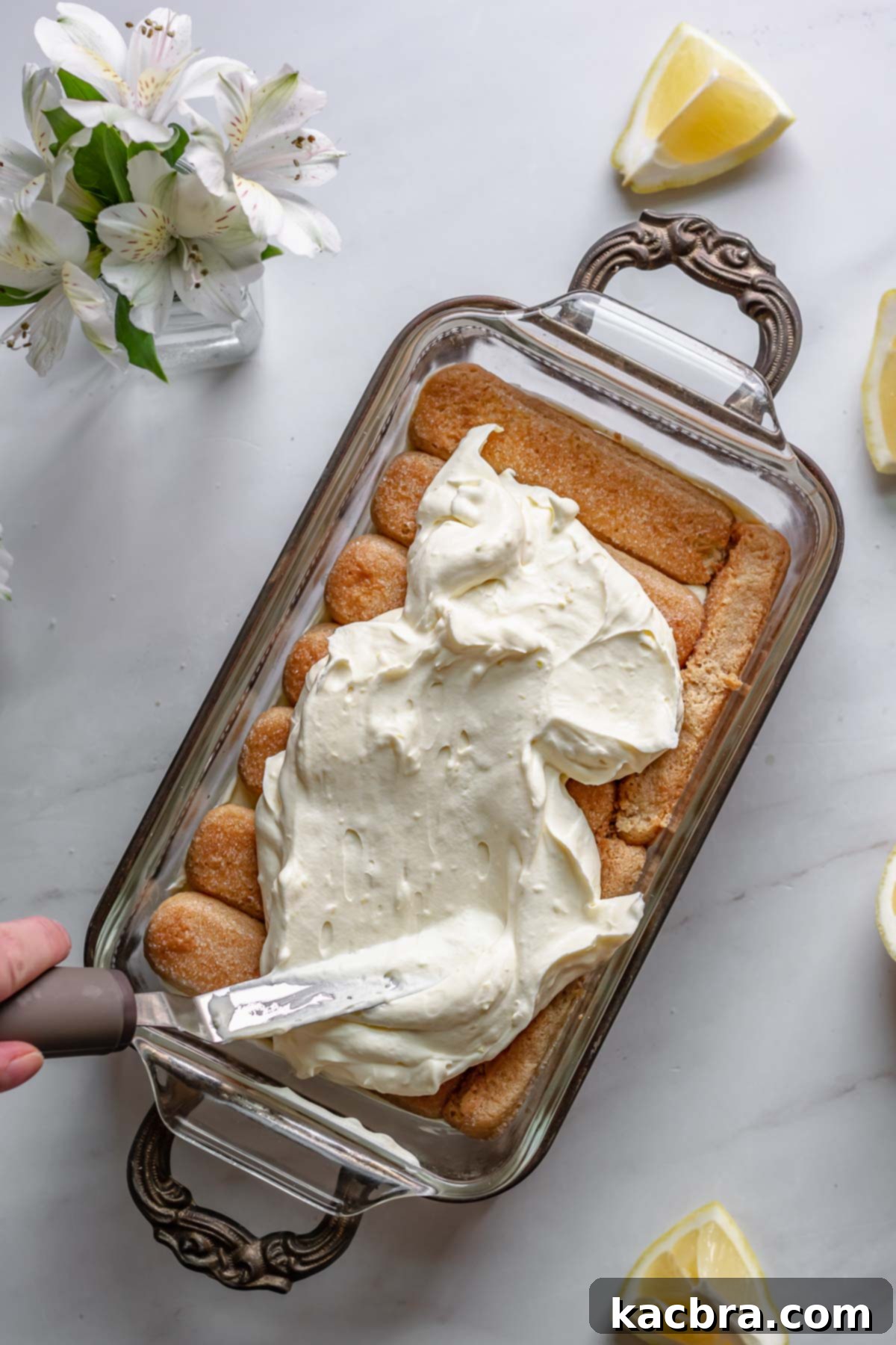 Spreading the remaining lemon cream smoothly over the top layer of lady fingers.