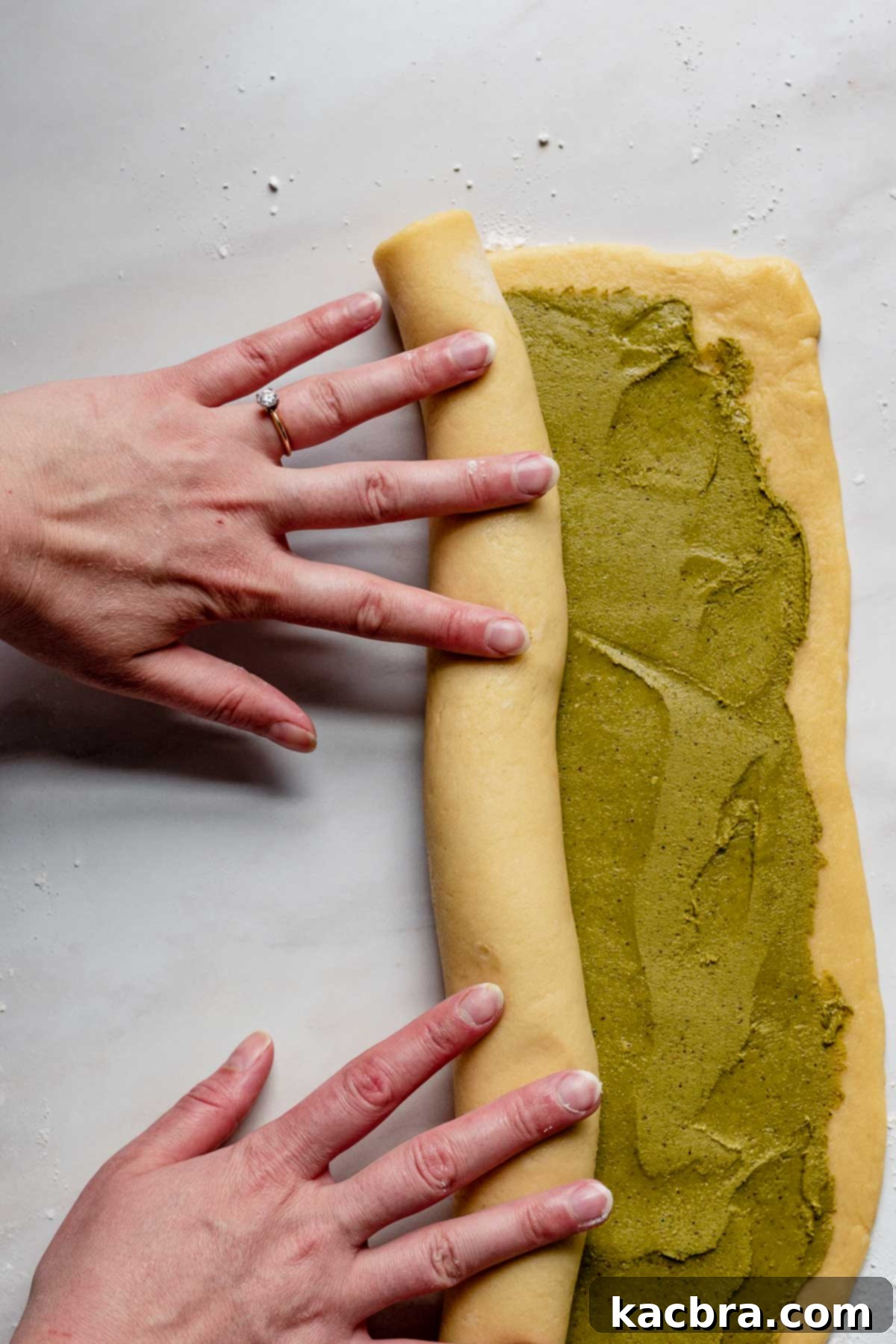 Hands carefully roll up the babka dough, starting from one of the long ends, creating a tight log filled with the rich pistachio mixture, ready for shaping.