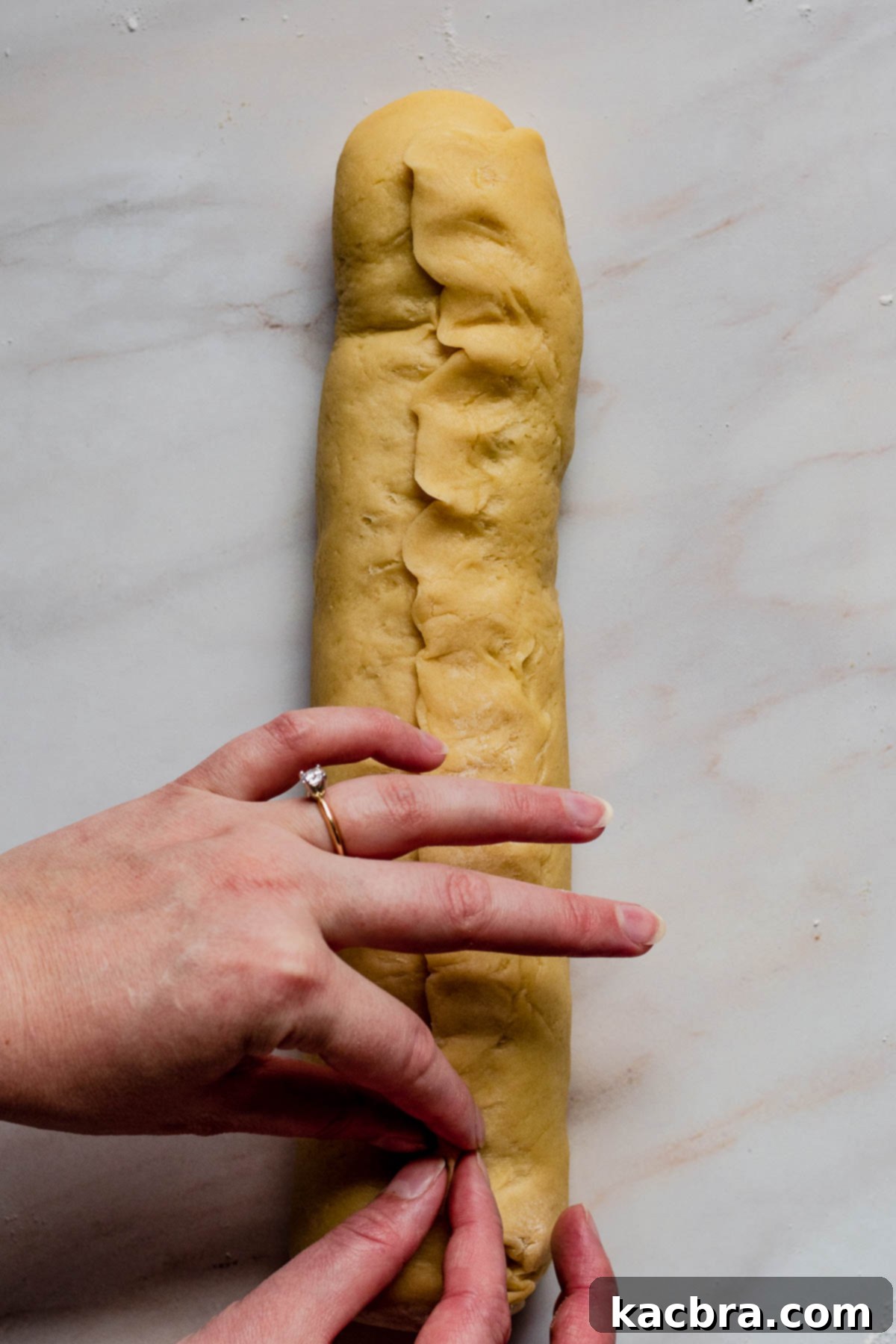A hand gently pinching the seam of the rolled babka dough shut, ensuring the filling is completely sealed within.