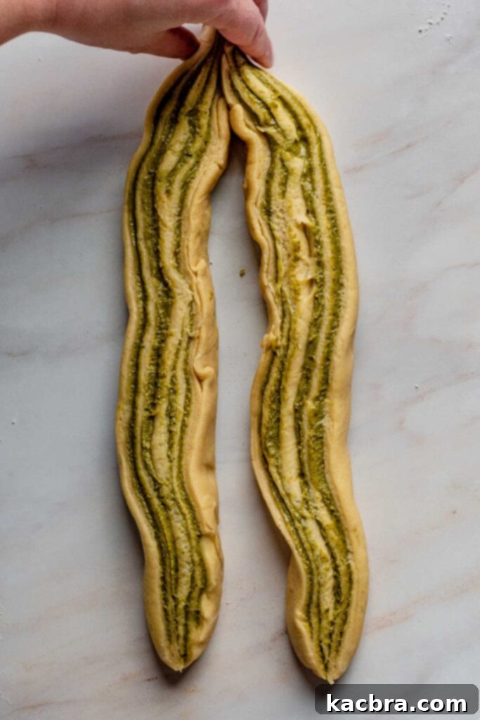 A hand gently pinches the top ends of the two cut babka dough strips together, securely joining them before twisting to form the classic babka braid.