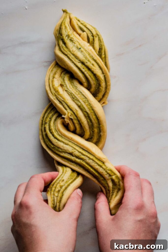 Hands carefully wrap and twist the two dough pieces around each other, ensuring the vibrant green filling sides remain facing up to create the characteristic babka swirl pattern.