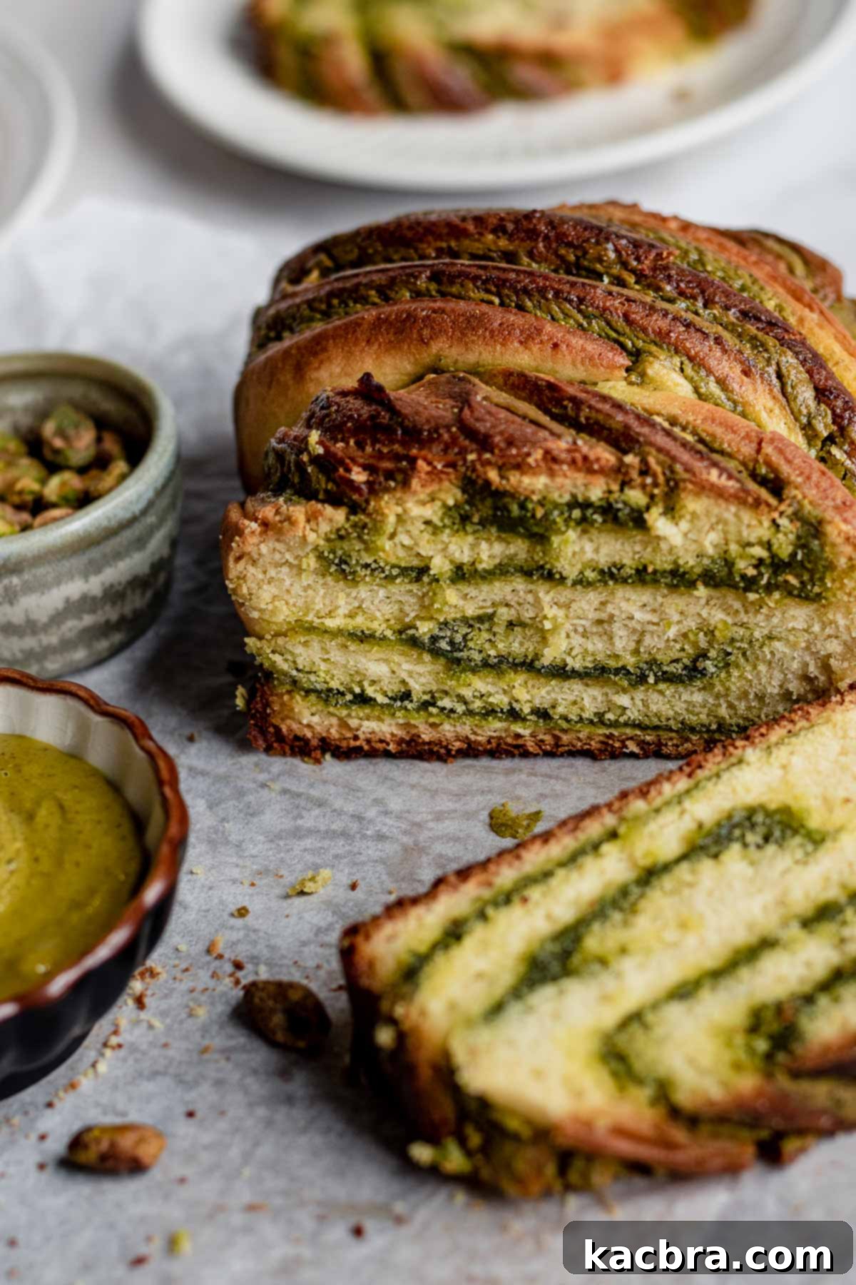 A beautifully baked pistachio babka loaf, perfectly golden with visible swirls of green filling, presented alongside a single tempting slice, inviting enjoyment.